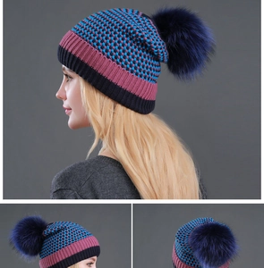 Detail view of winter knit beanie with real raccoon fur pom and multicolor plaid pattern