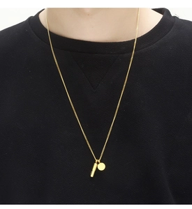 Detalle de un collar con colgante de cápsula minimalista bañado en oro en fondo negro mate