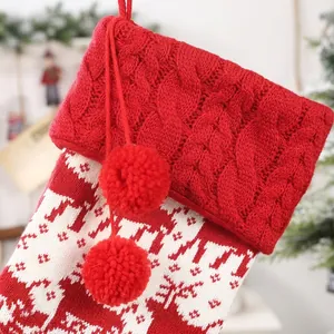 Close-up of knit Christmas stocking featuring red pom poms and white reindeer patterns