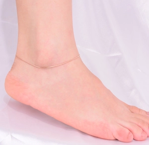 Detail shot of a minimalist rose gold snake chain anklet on a model's ankle