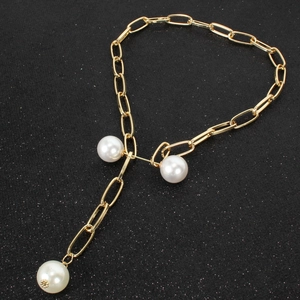 Minimalist gold chain necklace with white pearls on a textured black background