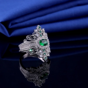 Macro shot of silver crown ring with green emerald stone on black mirror