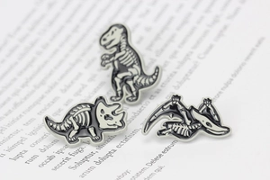 Macro shot of three zinc alloy dinosaur skeleton enamel pins on a vintage book page
