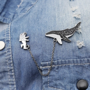 Detail of creative astronaut and whale enamel pins connected by chain on denim jacket