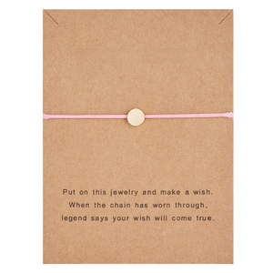 Detail of pink woven wish bracelet with a gold charm on a Make a Wish display card