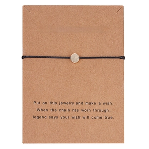 Detailed view of woven wish bracelet with textured gold charm on kraft card packaging