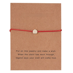 Minimalist red cord wish bracelet with gold circular charm on brown kraft paper card