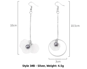 Détails de longues boucles d'oreilles argentées asymétriques avec pétales blancs et perles