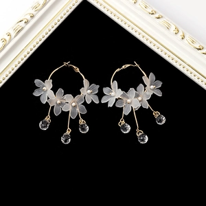 Détail de boucles d'oreilles dorées avec fleurs givrées et gouttes de cristal