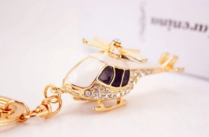 Detail of a golden metal helicopter keychain with white enamel and sparkling crystals