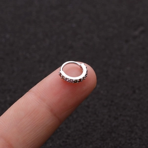 Nahaufnahme eines silbernen Nasenpiercings mit Zirkon-Pavé-Fassung auf einer Fingerspitze