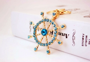 Macro shot of gold ship wheel keychain with blue crystals on white background