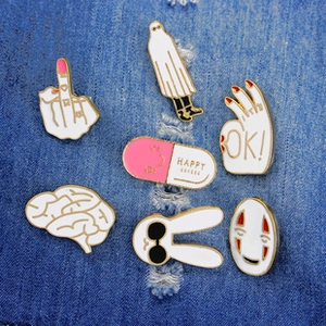Detail of 7 cartoon enamel pins including No-Face and ghost on blue denim fabric background