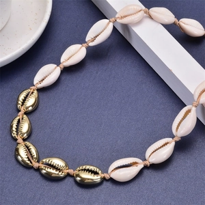 Macro detail of natural white and gold plated shell necklace on beige braided rope