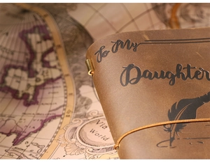 Close-up of vintage brown leather notebook with 'To My Daughter' feather engraving and strap