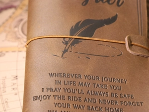 Close-up of vintage brown leather journal with embossed quote and elastic closure strap