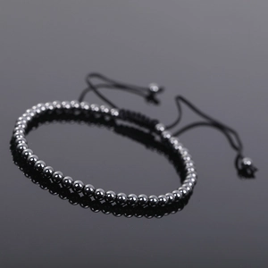 Macro detail of hematite beaded bracelet with adjustable black braided rope on black surface