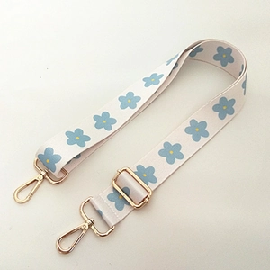 Close-up of adjustable white bag strap with blue flower patterns and gold metal clips