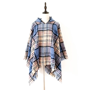 Dettaglio di un poncho con cappuccio a quadri blu con morbide frange su un manichino