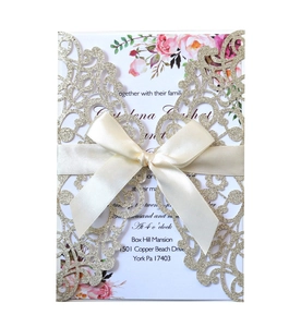 Detailed laser-cut gold glitter wedding invitation with white ribbon bow and floral card