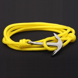 Close-up of yellow braided nylon rope bracelet with silver anchor clasp on dark surface