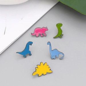 Detailed view of five colorful dinosaur enamel pins in pink green blue and yellow shades