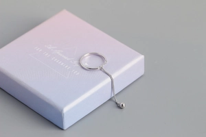 Detail of S925 sterling silver tassel ring with dangling bead on a gift box corner