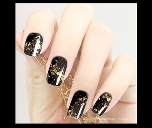 Gros plan d'ongles noirs brillants avec des flocons de feuilles d'or et effet marbré