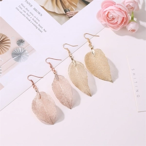 Detail shot of hollow leaf dangle earrings in gold and rose gold on a minimalist setup