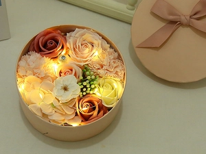 Round floral gift box with soap roses, carnations, LED string lights and a bow