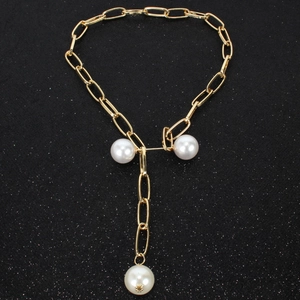 Close-up of golden paperclip chain necklace with three white faux pearls on a black background