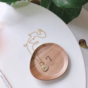 Detail of vintage gold coin pendant necklace on a wooden tray with minimal aesthetic