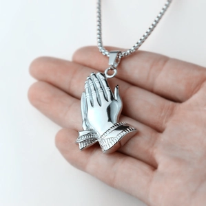 Macro view of silver praying hands pendant necklace held in hand to show metallic detail