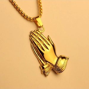 Close-up of golden praying hands pendant with detailed texture on a plain background