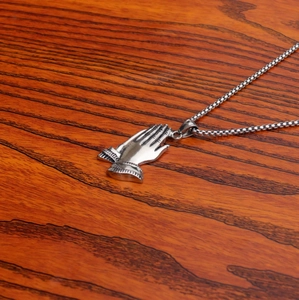 Detailed view of silver stainless steel praying hands pendant on a wooden surface