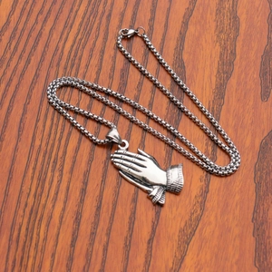 Detailed view of silver prayer hands pendant on box chain over a wood surface