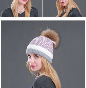 Detail of a knit beanie featuring a grey white pink pattern and a large brown faux fur pom