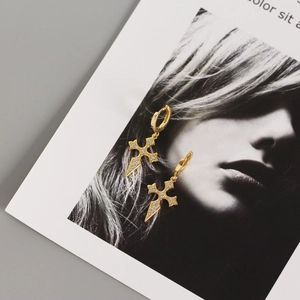 Detailed view of gold cross stud earrings with diamonds on a magazine background