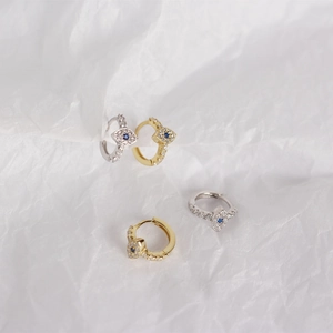 Detailed macro view of gold and silver S925 sterling silver evil eye hoop earrings with blue gems