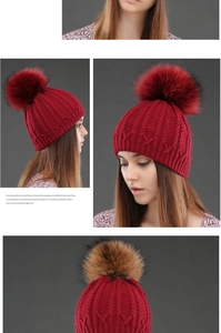 Close-up of deep red winter cable knit beanie featuring a thick raccoon fur pom-pom detail
