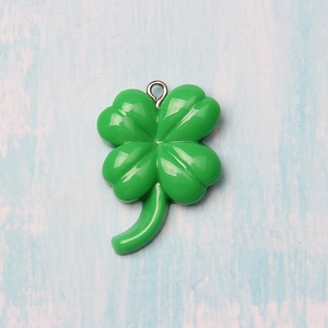 Green resin four-leaf clover charm with metal ring on light blue wood background