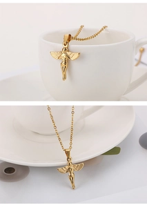 Detail view of a gold angel wing pendant necklace draped over a white ceramic cup