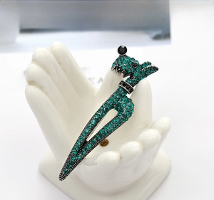 Detail shot of a green and black rhinestone poodle brooch on a white hand display stand