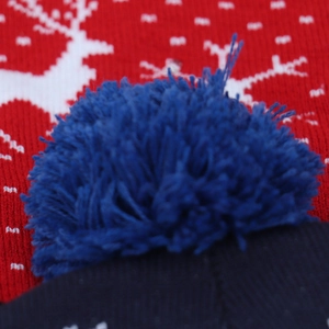 Close-up of blue pom-pom on red knitted Christmas hat with festive snowflake patterns