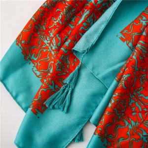 Close-up of turquoise satin shawl featuring intricate red floral patterns and tassel edges