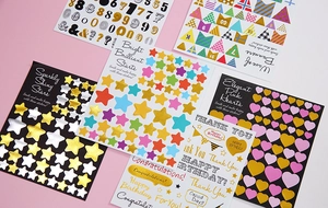 Close-up of decorative gold foil stickers featuring stars, hearts, and banners for DIY scrapbooking