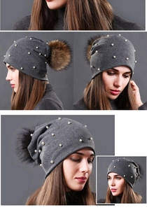 Detail of dark grey knit beanie featuring white pearls and a fluffy faux fur pom-pom
