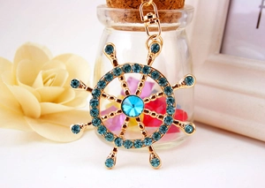 Detailed view of a golden nautical ship wheel keychain with sparkling blue crystals