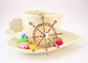 Close-up of golden nautical ship wheel pendant with sparkling crystals on a heart cup