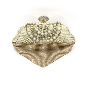 Detail of luxury gold evening clutch with white pearls and sparkling rhinestone tassels